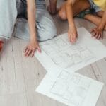 Para omawia plany domu rozłożone na jasnej drewnianej podłodze