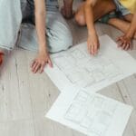 Para omawia plany domu rozłożone na jasnej drewnianej podłodze