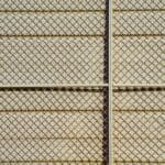 Detal siatki ogrodzeniowej rzucającej cienie w geometryczny wzór